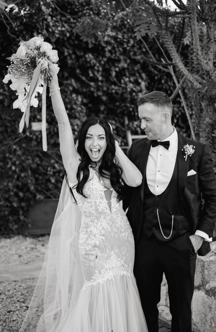 Bride raising her bouquet in celebration beside the groom